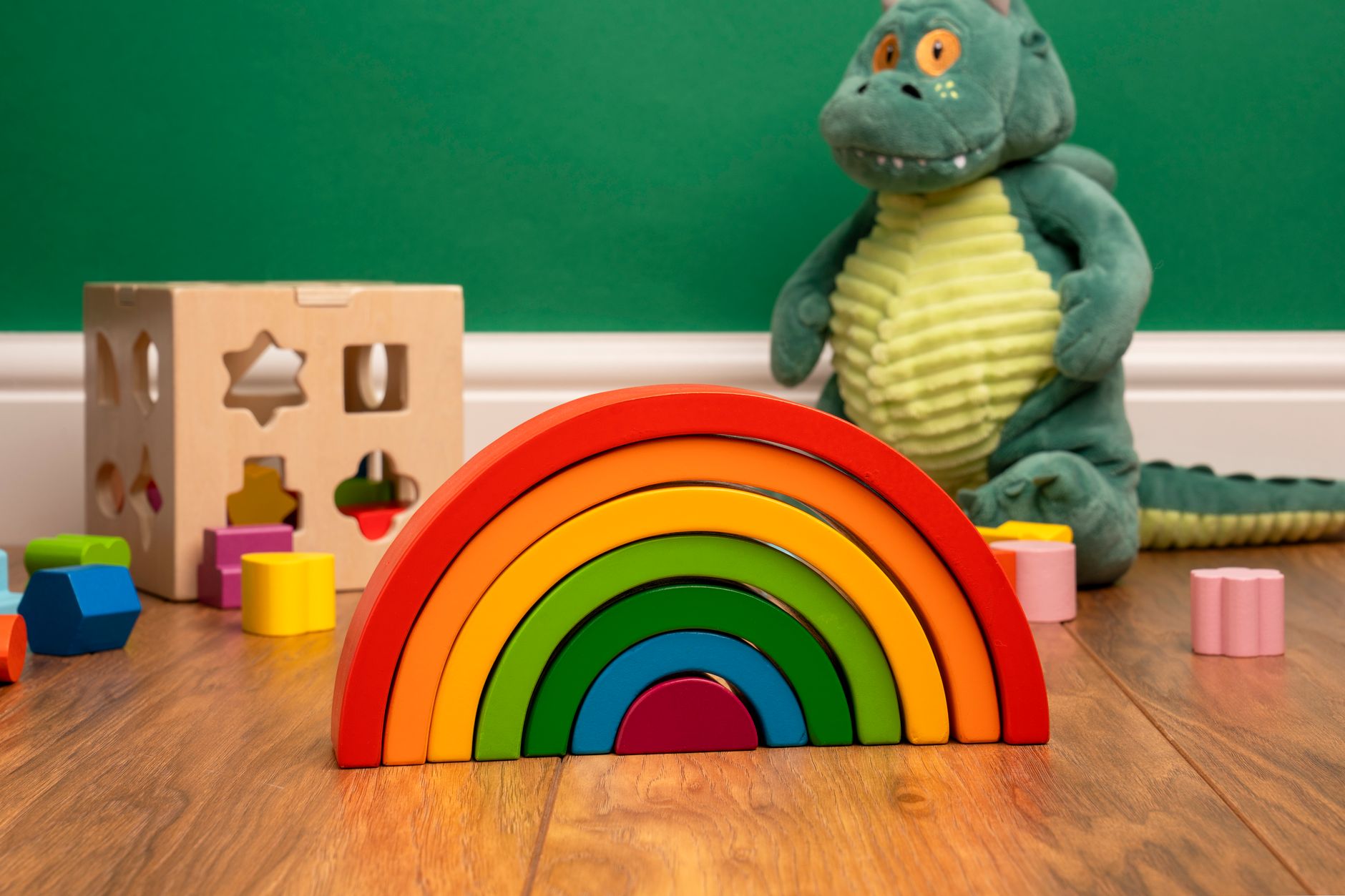 A vibrant wooden rainbow and dinosaur plush in a colorful playroom setting.