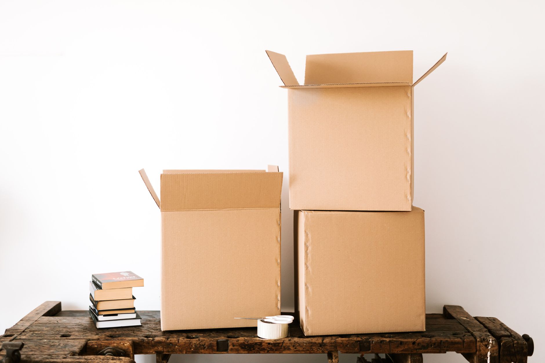Opened cardboard boxes and stack of books placed on wooden shabby table near tape with sci